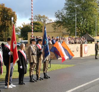 na zdjeciu widać poczet sztandarowy, w tle na podium zgromadzeni goście