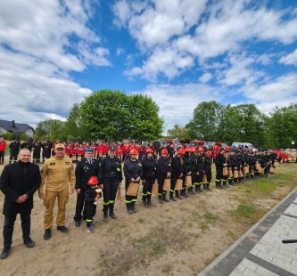 Zdjęcie przedstawia zakończenie zawodów podczas dekoracji: Wójt wraz z dużą grupa uczestników i zaproszonych gości ze środowiska pożarniczego.