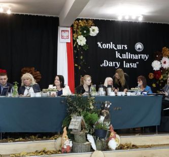 na zdjęciu widać komisję konkursową siedzącą przy stole, za nimi hasło konkursu